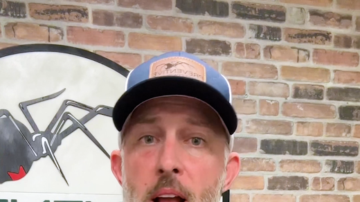 A bearded man in a blue polo shirt and hat speaks into a lapel mic. Behind him, a brick wall displays a black widow spider logo and upside-down text: "ADVENT CONTROLS."
